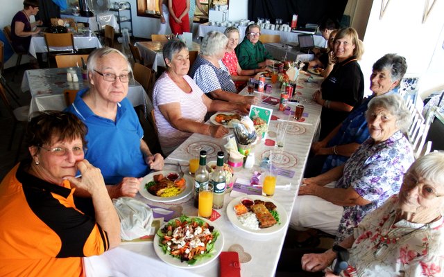 Enkele Gansbaaiers sit gesellig om ‘n tafel en eet tydens die Kersmark, met Maretha Geldenhuys voor links